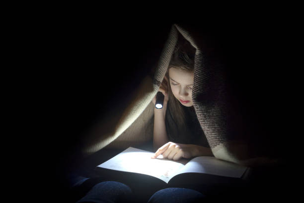 una chica con una linterna leyendo un libro. - child bedtime imagination dark fotografías e imágenes de stock