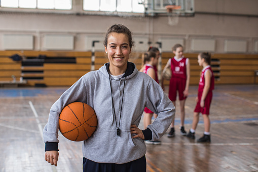 Female coach practicing with basketball team on basketball court