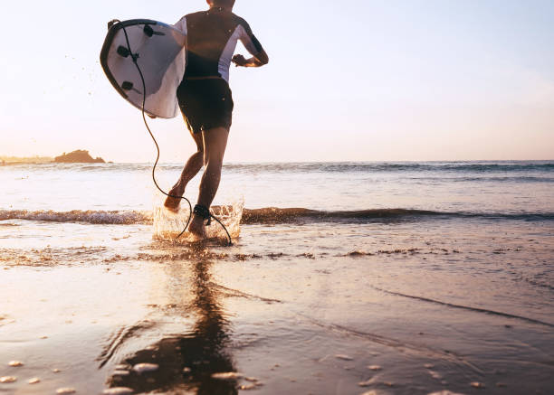 istock Young man Surfer taking surfboard and running with long surf board to waves on the evening sunset sky background. Active holidays spending concept. 1131658110