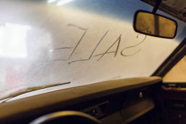 istock Inside view of old broken car interior with dusty vehicle dashboard, back mirror, driving steering wheel and dirty wind screen with title SALE written outside. Concept of sale pre-owned cars on the repair parts. 1131658928