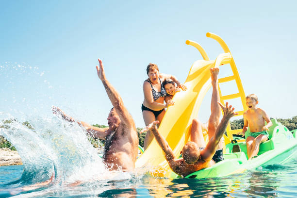 felice famiglia pazza mani su galleggiante playground slide catamaran mentre si godono il viaggio in mare mentre hanno le vacanze estive - lake summer beach nautical vessel foto e immagini stock