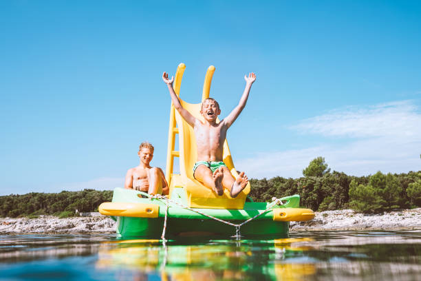 kleiner junge rutscht in das meerwasser von schwimmenden playground dia catamaran, während sie genießen seereise mit seinem bruder - pedal boat stock-fotos und bilder