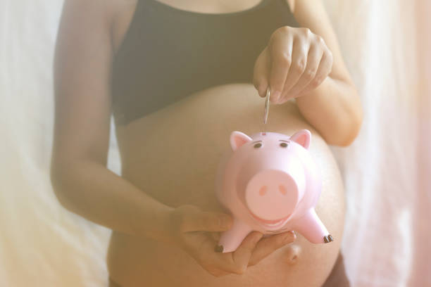 妊娠中の女性が貯金箱にお金を入れる - human pregnancy finance mixed race person holding スト��ックフォトと画像