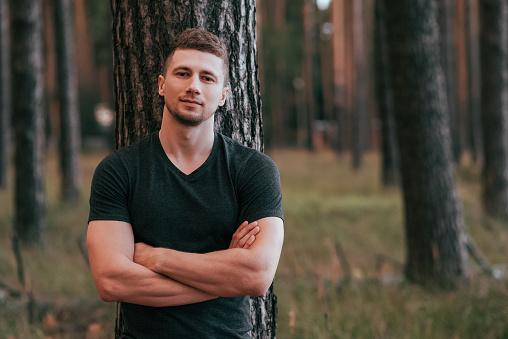 Male athlete posing in the woods on a background of a tree behind his back. Active lifestyle fitness, workout on the street. Powerful confident and strong pumped guy. Free space for text.