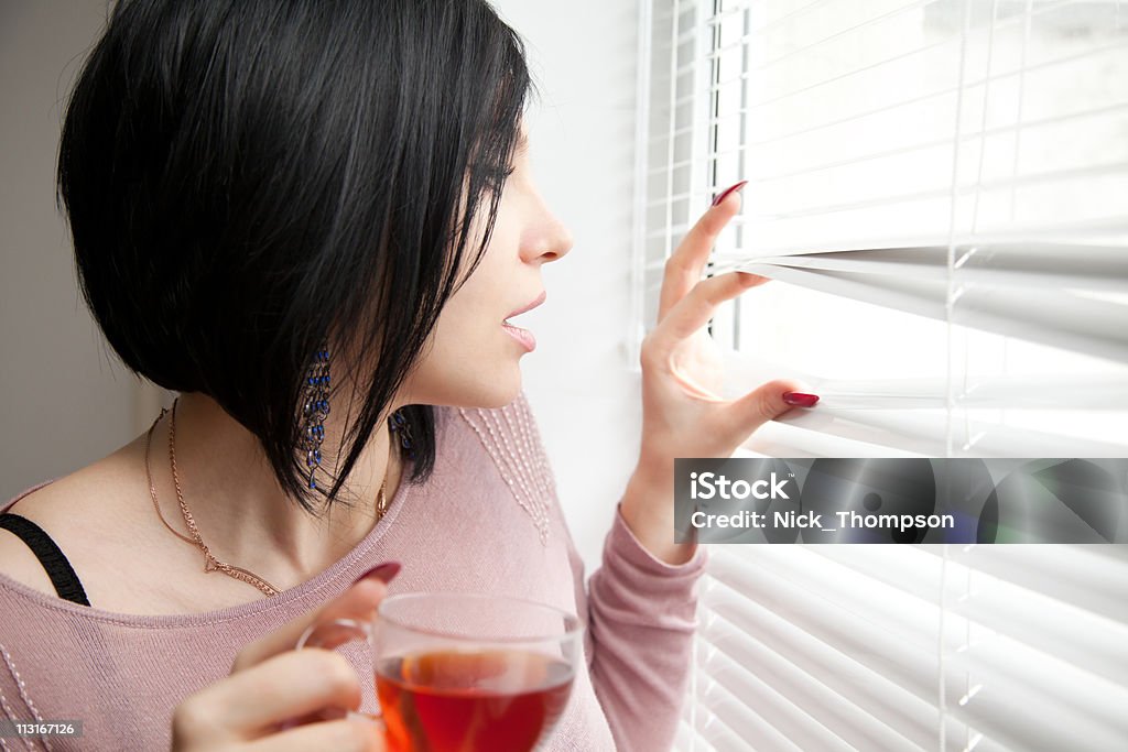 Brunette con una taza en sorpresa peeping a través de las persianas - Foto de stock de Adulto libre de derechos