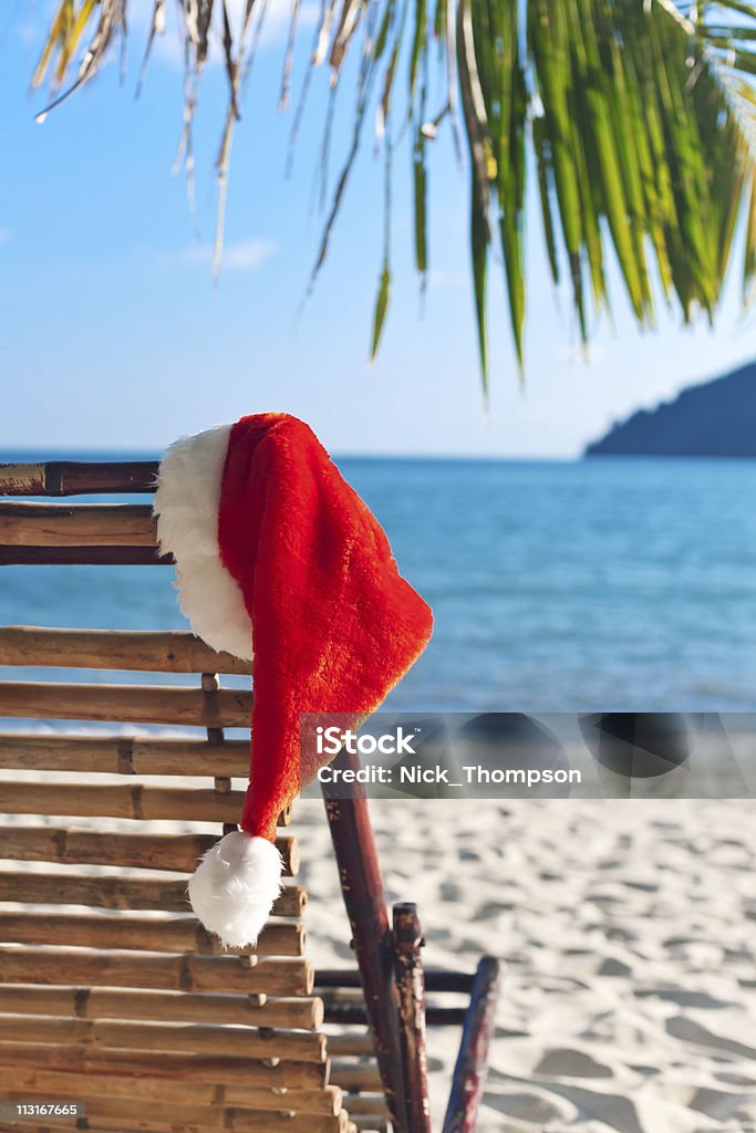 Santa's Red hat colgar en una silla de playa bajo una palmera - Foto de stock de Aire libre libre de derechos