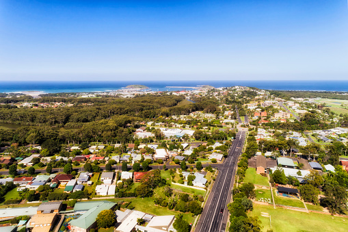 Aerial view over local regional town Coffs Harbour on Australian Middle North Coast of NSW towards Pacific ocean waterfront over local suburbs, streets, houses and parks.