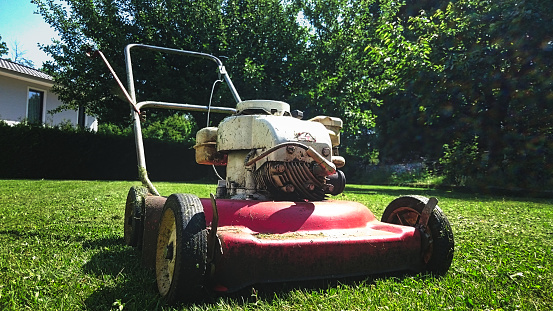 Old red lawn mower on green grass of backyard meadow in sunlight