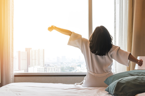 Simple city lifestyle happy woman waking up in the morning taking some rest relaxing in luxury comfy city hotel room