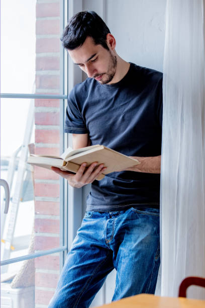 istock Young man with book staying near window 1131687598