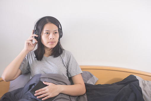 beautiful Asian woman listening music with headphone relaxing on the bed