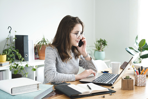 Mujer de negocios joven trabajando en el ordenador portátil y hablando teléfono móvil en la oficina. photo