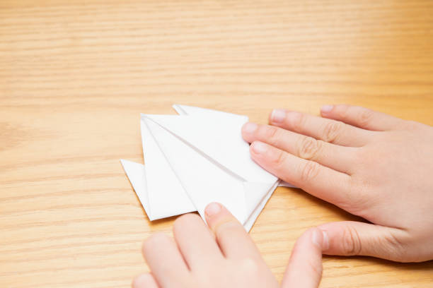 kid folding an origami frog by white paper