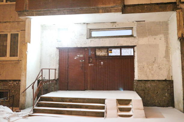 Dark back street with brick building in winter night in warm street light close up. Snowfall on backstreet with copy space. Urban snowy road. Cityscape in snow weather. Escape ladder with back door.