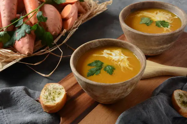 Sweet potato and carrot soup served with sour cream in wooden bowl. Orange vegetable soup concept. Vegan food