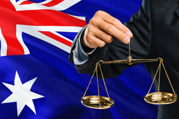 o juiz australiano está prendendo escalas douradas de justiça com fundo de ondulação da bandeira de austrália. tema da igualdade e conceito legal. - ozzie - fotografias e filmes do acervo