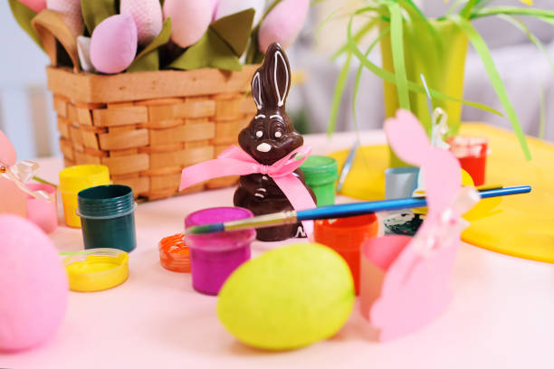 chocolate Easter Bunny on the background of Easter decor, flowers, painted eggs, cans with paint. Preparing for the celebration of Easter
