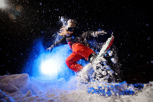 Female snowboarder dressed in a orange sportswear jumping on the mountain slope