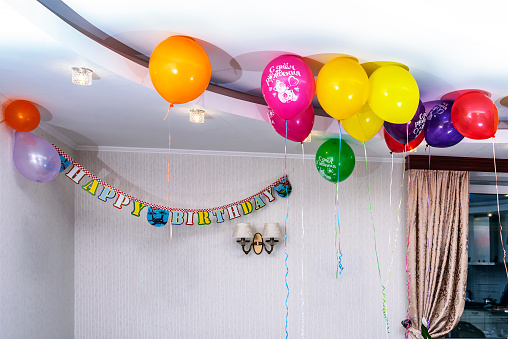 Festive background of decorated room with balloons under the ceiling. Birthday party concept. The inscriptions on the balloons in Russian: 