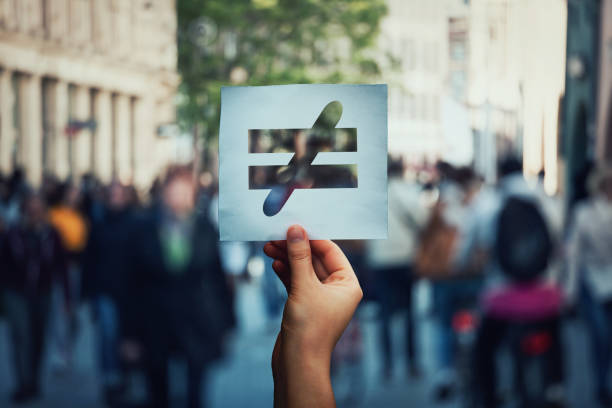 inequality social problem Human inequality as global social issue. Stop discrimination on grounds of race, sex or religion as hand holding a paper sheet with injustice, unfairness symbol over crowded street background. unfairness photos stock pictures, royalty-free photos & images