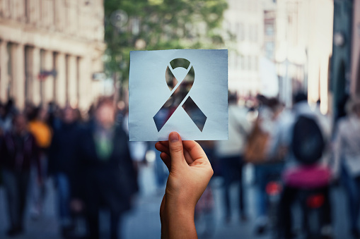 Global issue stop AIDS as hand holding a paper sheet with HIV red ribbon symbol over crowded street background. Fight against cancer concept, substance abuse and anorexia awareness.