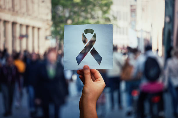 stop aids Global issue stop AIDS as hand holding a paper sheet with HIV red ribbon symbol over crowded street background. Fight against cancer concept, substance abuse and anorexia awareness. hiv photos stock pictures, royalty-free photos & images