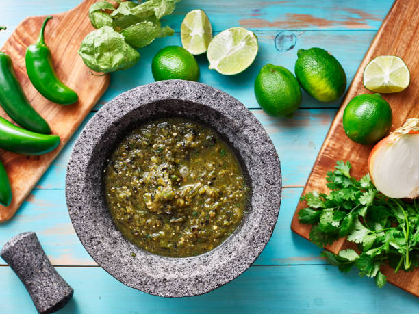 salsa verde in stone molcajete flat lay composition salsa verde in stone molcajete flat lay composition on blue rustic boards tomatillo photos stock pictures, royalty-free photos & images