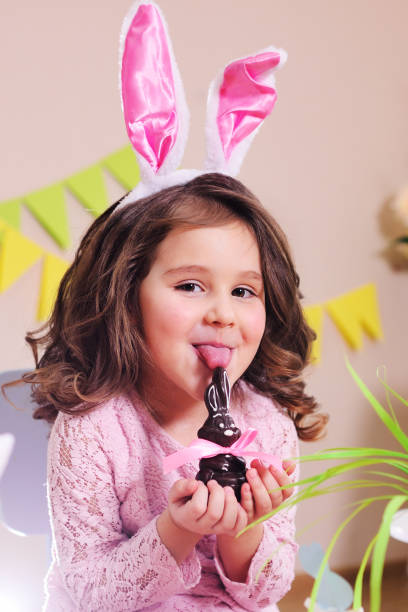 baby girl licks a chocolate Easter bunny stock photo
