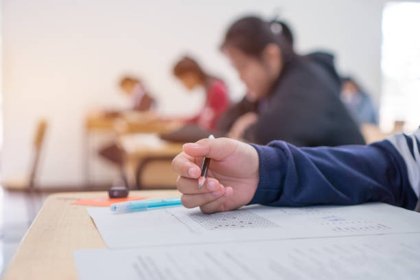 exams test student in high school, university student holding pencil for testing exam writing answer sheet and exercise for taking in assessment paper on wood table classroom. education study concept - exam imagens e fotografias de stock