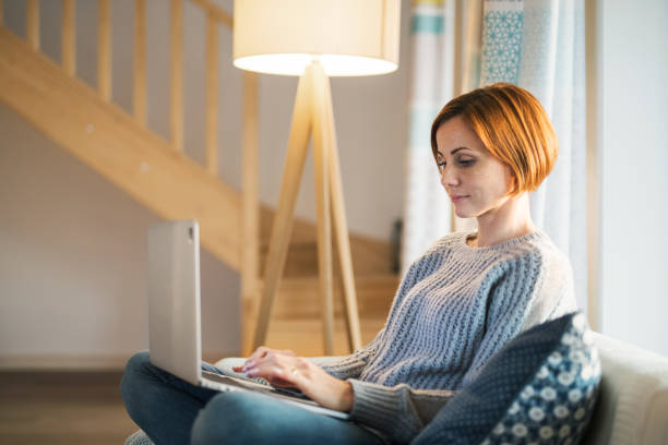 A young woman sitting indoors on a sofa at home, using laptop.