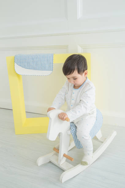 istock Baby boy playing with a rocking horse on grey background 1131762280