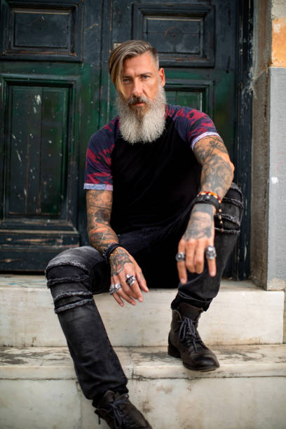 Portrait Of A Bearded Tattooed Attractive Man Who Is Sitting On A Stairways  On Front A Old Wooden Door Stock Photo - Download Image Now - iStock