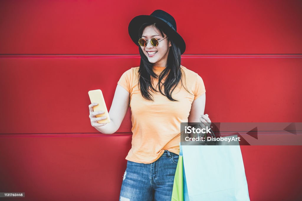 Happy trendy asian girl using shopping app holding bags outdoor - Young woman having fun buying new clothes on web with smartphone - Retail, tech, sales and buyer addiction concept - Focus on face Retail Stock Photo