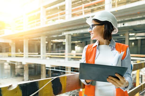 portrait du constructeur féminin adulte, ingénieur, architecte, inspecteur, directeur au chantier de construction. femme avec le plan, tablette numérique - architect female women construction photos et images de collection