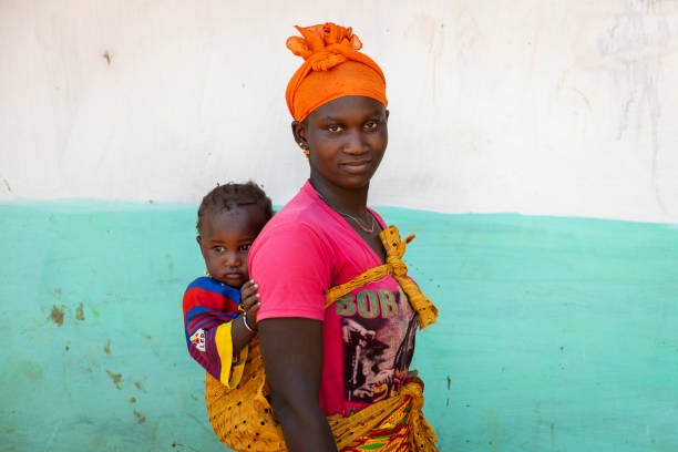 Portrait of of a woman carrying her baby daughter on her shoulders, in the village of Mandina Mandinga in the Gabu Region Gabu Region, Republic of Guinea-Bissau - February 7, 2018: Portrait of of a woman carrying her baby daughter on her shoulders, in the village of Mandina Mandinga in the Gabu Region, Guinea Bissau poverty child ethnic indigenous culture stock pictures, royalty-free photos & images