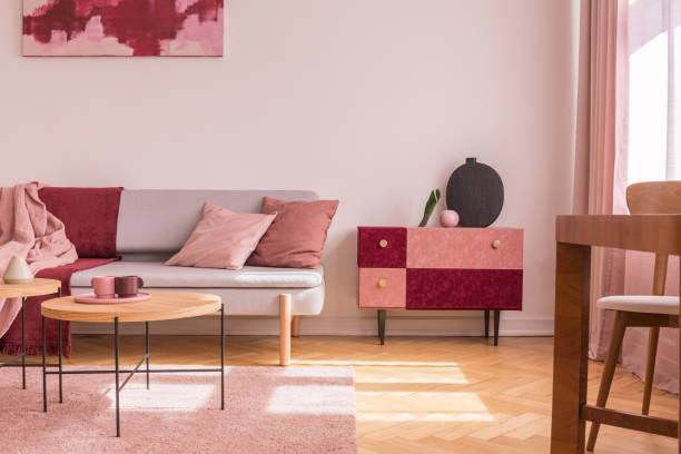 istock Fancy suede covered cabinet with black stylish vase next to comfortable grey sofa with pastel pink pillow and blanket 1131772370