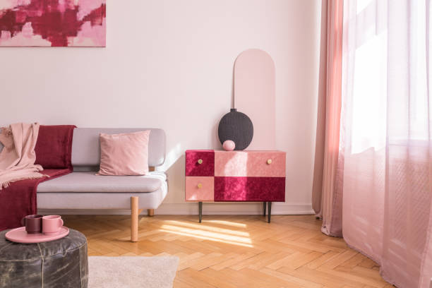 istock Chic suede covered cabinet with black trendy vase next to comfortable grey couch with pastel pink pillow and burgundy blanket 1131772381
