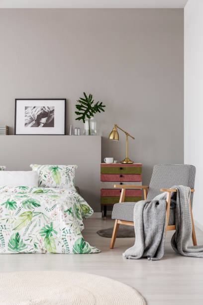 istock Patterned armchair with grey blanket in trendy bedroom interior with comfortable bed with floral bedding 1131772950