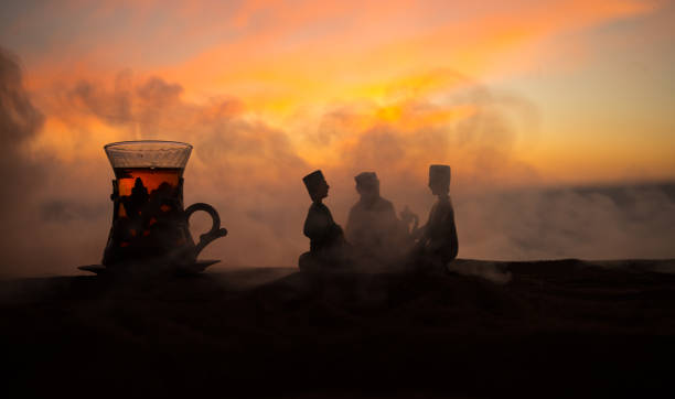 istock Arabic tea in traditional glass and pot on desert at sunset. Eastern tea concept. Artwork decoration on sand with tea. 1131773334