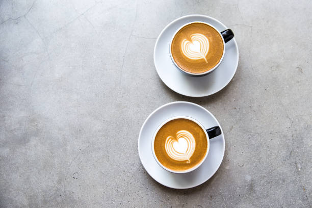 Two black cups of tasty cappucino with love art latte. Two white cups of tasty cappucino with heart art latte. Concrete grey backdrop. milk froth stock pictures, royalty-free photos & images