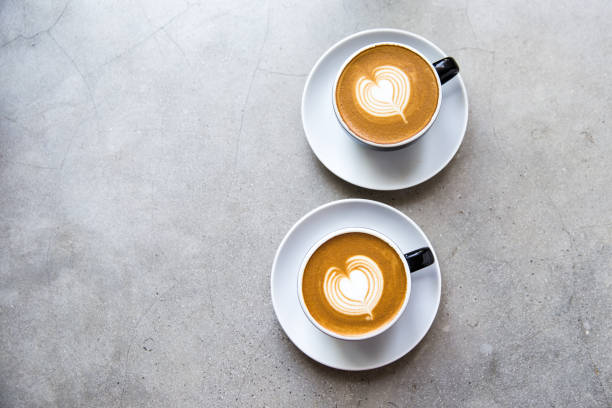 dois copos pretos do cappucino saboroso com latte da arte do amor. - latté cafe froth art cup - fotografias e filmes do acervo