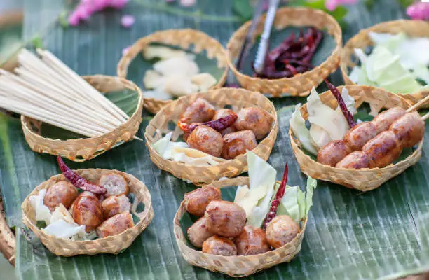 Photo of Sausage small circles on the grid-iron grill with smoke over charcoal. Thai sausage, fermented rice with pork sausage served with vegetables.