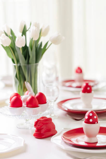 istock Happy easter. Decor and table setting of the Easter table is a vase with white tulips and dishes of red and white color. Easter colored eggs with white polka dots. 1131791483