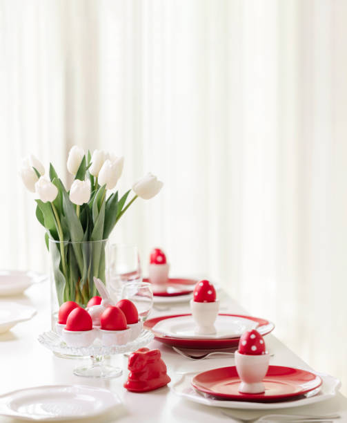 istock Happy easter. Decor and table setting of the Easter table is a vase with white tulips and dishes of red and white color. Easter colored eggs with white polka dots. 1131791488