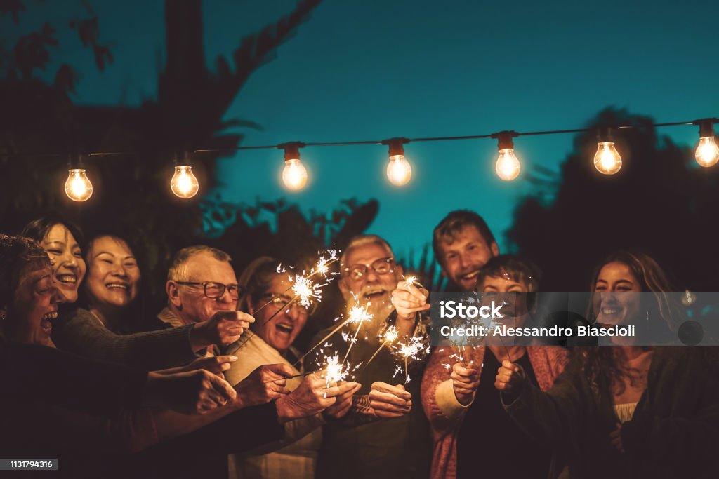 Famiglia felice che festeggia con scintillio di festa notturna all'aperto - Gruppo di persone con diverse età ed etnia che si divertono insieme all'esterno - Concetto di amicizia, vigilia e celebrazione - Foto stock royalty-free di Famiglia