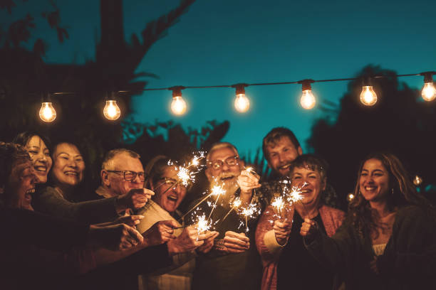夜のパーティーアウトドアで線香花火で祝う幸せな家族-異なる年齢や民族を一緒に楽しんでいる人々のグループ-友情、イブとお祝いの概念 - スペイン 写真 ストックフォトと画像