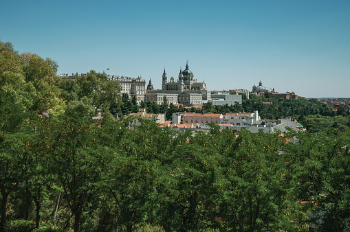 Landscape with the Royal Palace and Almudena Cathedral on the horizon amidst green treetops, in a sunny day at Madrid. Capital of Spain this charming metropolis has vibrant and intense cultural life.