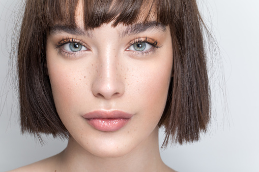 Close up studio shot of a beautiful girl with short brown hair, freckles and soft make up.