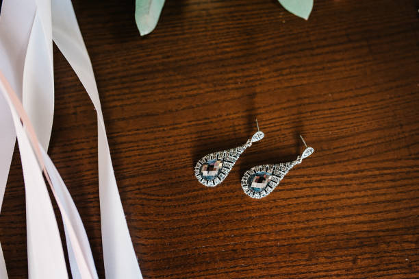 Wedding accessory bride. Stylish silver diamond earrings, flowers on table standing on wooden background. flat lay. top view.