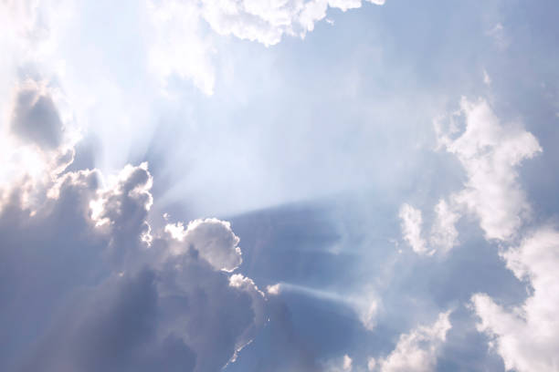 istock Clouds and sun shines through rays of light in the illuminated picturesque sky. 1131809410